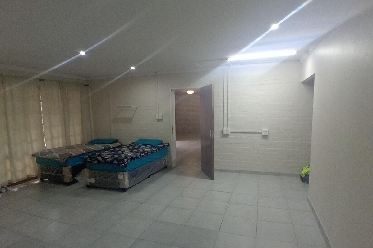 A spacious bedroom featuring tiled flooring, recessed lighting, and painted brick walls with exposed electrical conduit.