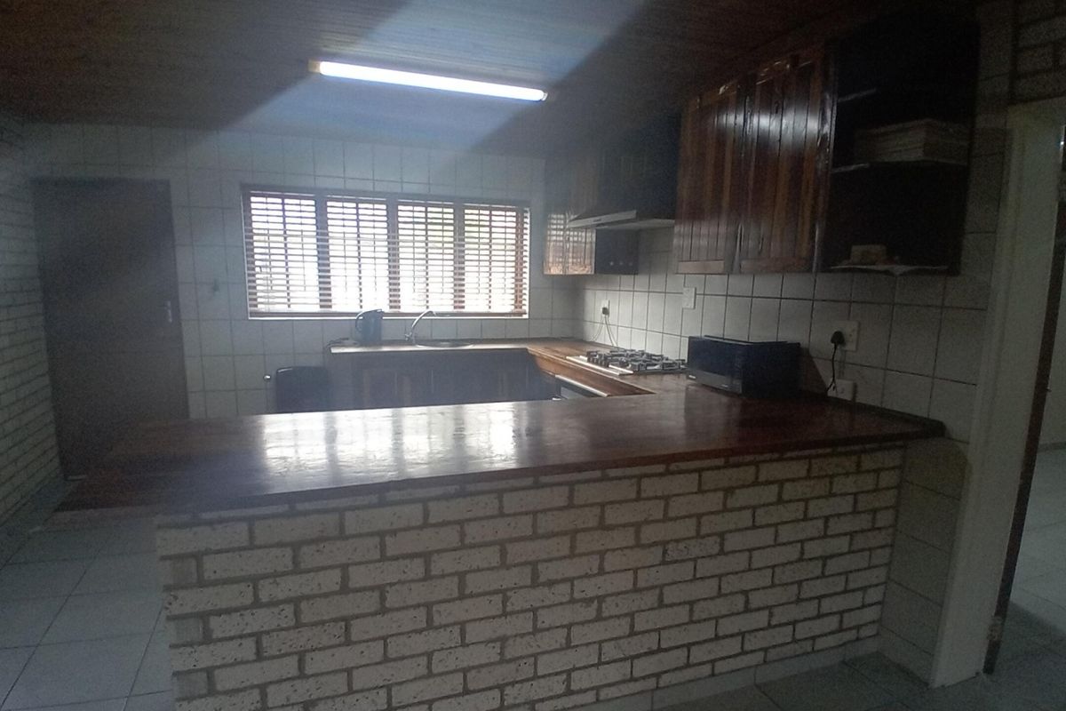 A functional kitchen featuring wooden cabinetry, a brick-based breakfast bar, tiled backsplash, and a gas hob with an extractor fan.