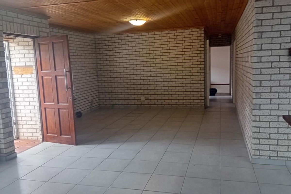 An empty living area featuring exposed brick walls, ceramic floor tiles, and a timber tongue and groove ceiling.