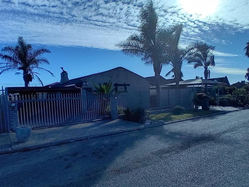 Front exterior view of a brick house featuring a secure metal gate, perimeter fencing, and a paved driveway.