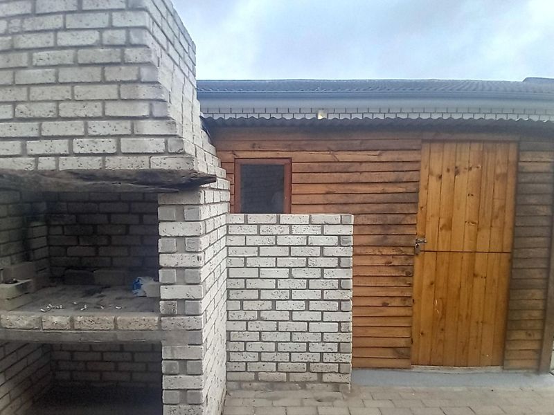 Outdoor entertainment area featuring a brick built-in braai and a timber-clad storage structure set on a paved patio.