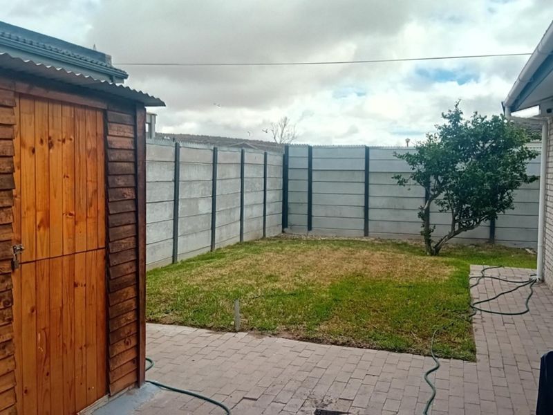 A rear garden area featuring a paved patio, a wooden storage shed, and a precast concrete boundary wall.