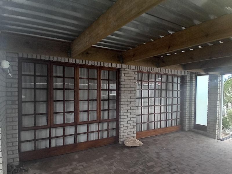 A covered outdoor patio area featuring brick walls, timber beam ceiling, and large timber-framed glass doors leading into the home.