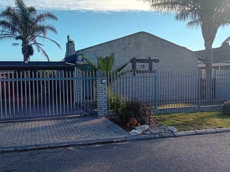 Front exterior view of a brick house featuring a paved driveway, carport, and secure metal perimeter fencing.