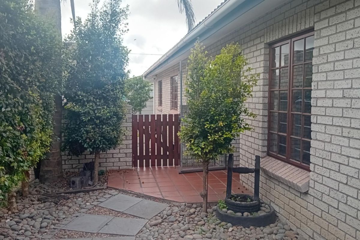 A rear exterior view of the house featuring a brick facade, tiled patio area, and a timber gate leading to the side yard.