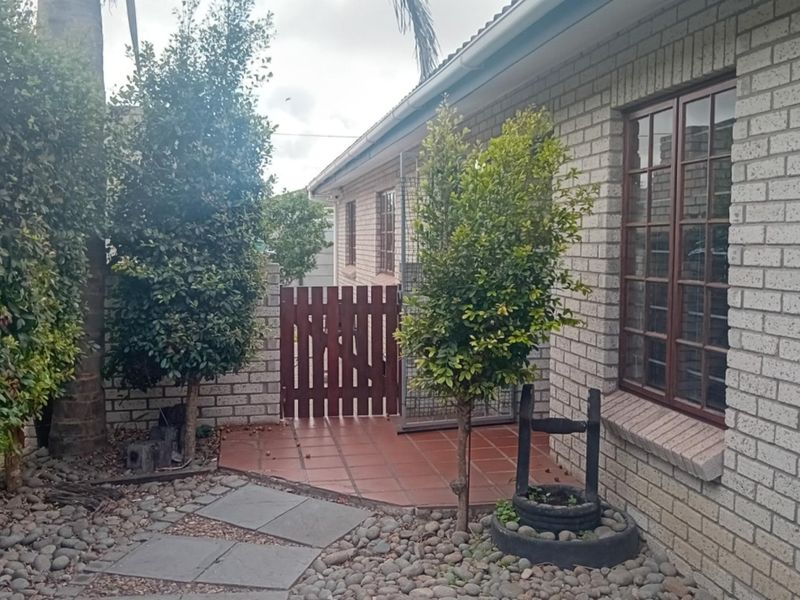 A rear exterior view of the house featuring a brick facade, tiled patio area, and a timber gate leading to the side yard.