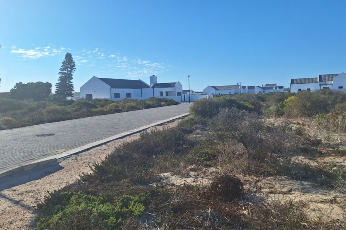 A view of a paved residential street in a coastal estate, featuring surrounding natural vegetation and established white-walled residential properties.