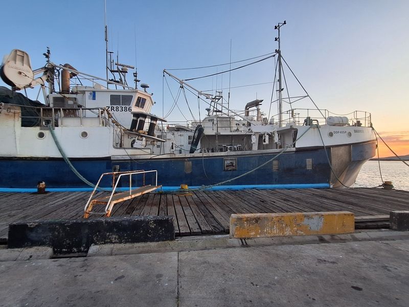 A view of a fishing vessel docked at a pier during sunset.