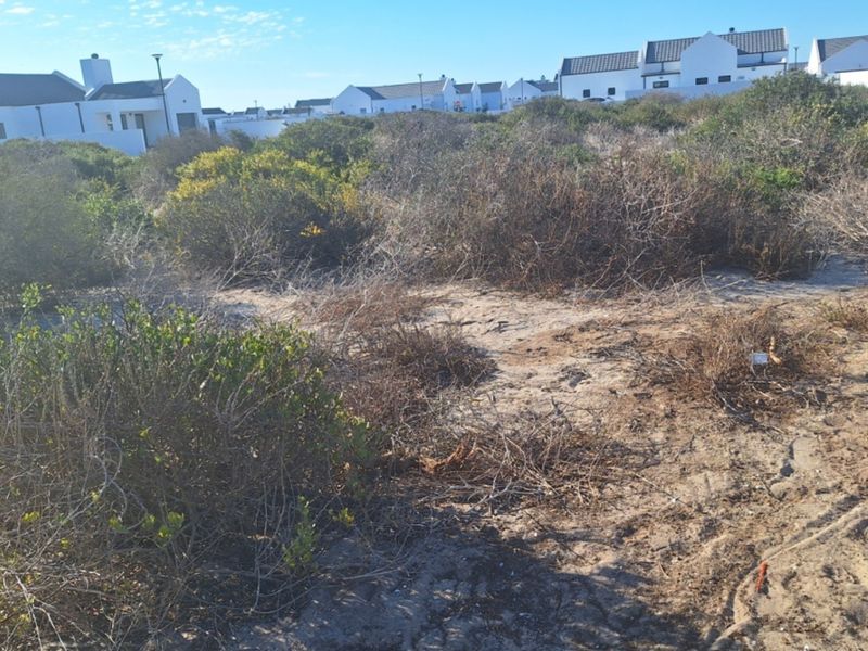 A vacant residential plot featuring sandy terrain and native coastal shrubbery, situated within a developed residential estate.