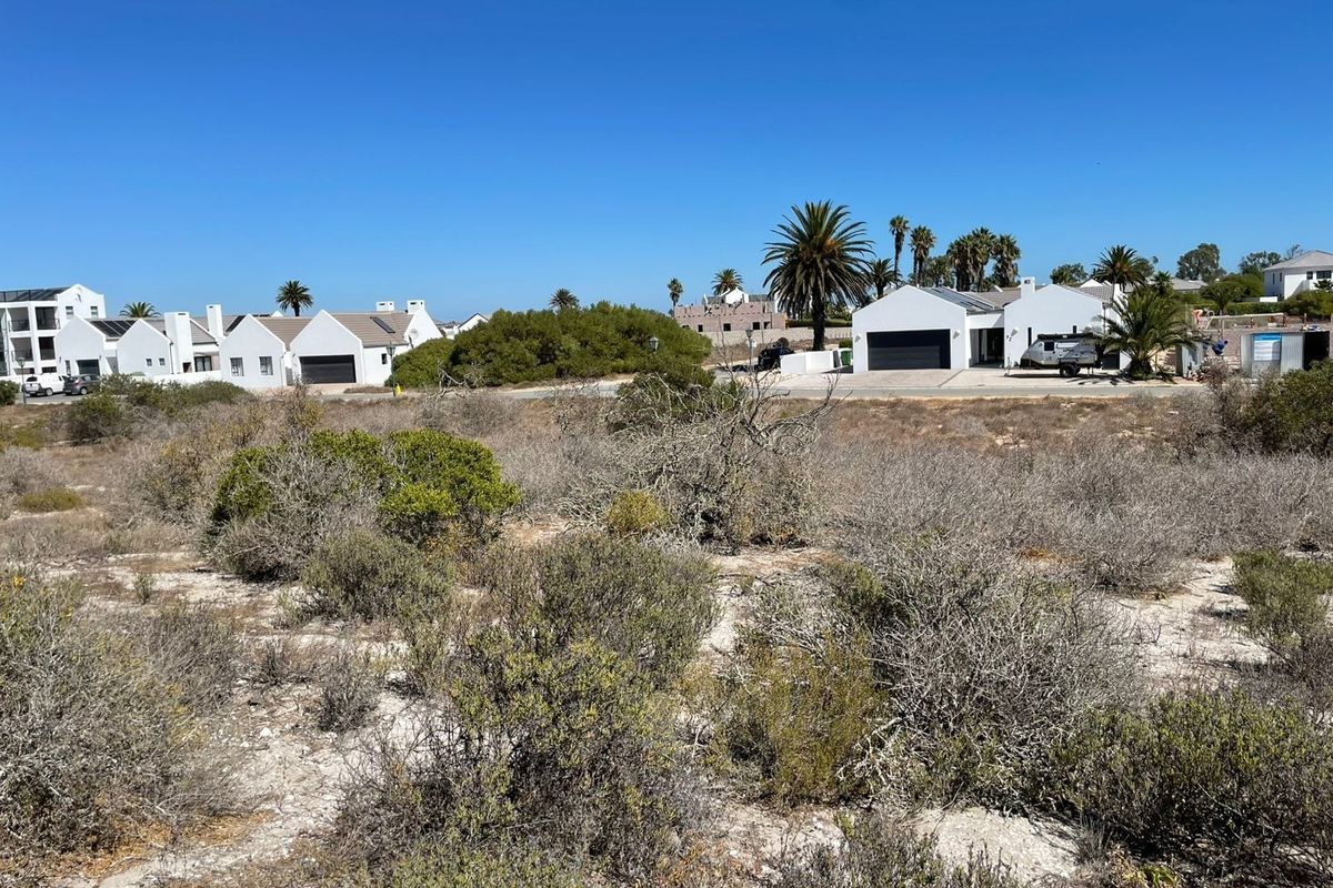 A view of a vacant residential plot featuring native coastal vegetation with established residential properties visible in the background.