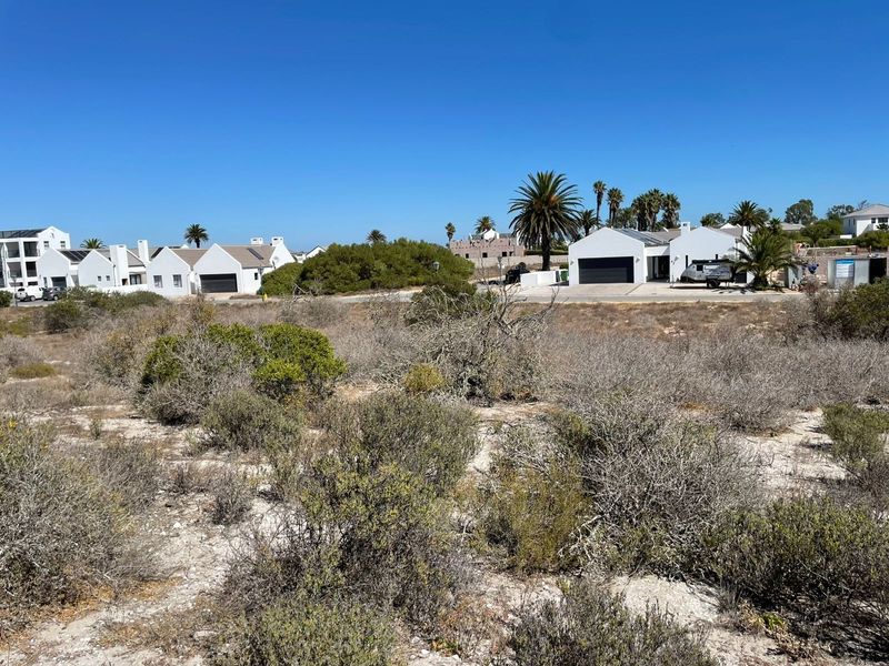 A view of a vacant residential plot featuring native coastal vegetation with established residential properties visible in the background.