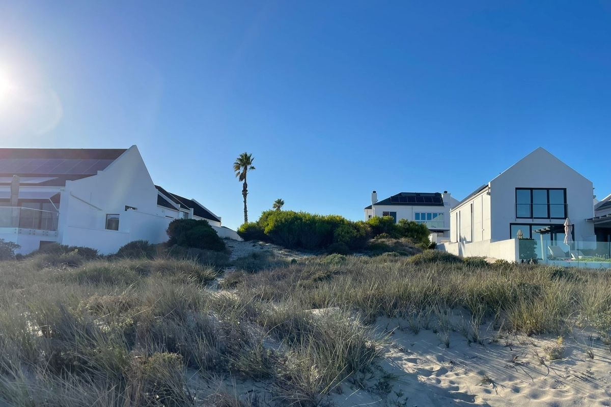 Rear view of coastal residential properties featuring white facades, solar panels, and glass balustrades, set against a natural sand dune landscape.