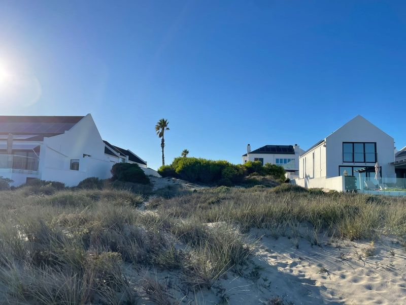 Rear view of coastal residential properties featuring white facades, solar panels, and glass balustrades, set against a natural sand dune landscape.