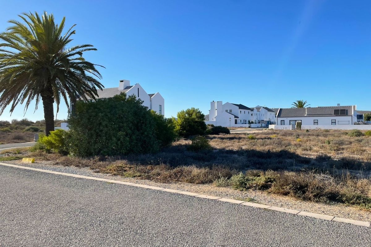A view of a vacant residential plot situated in a developed neighborhood with paved road access and established landscaping.