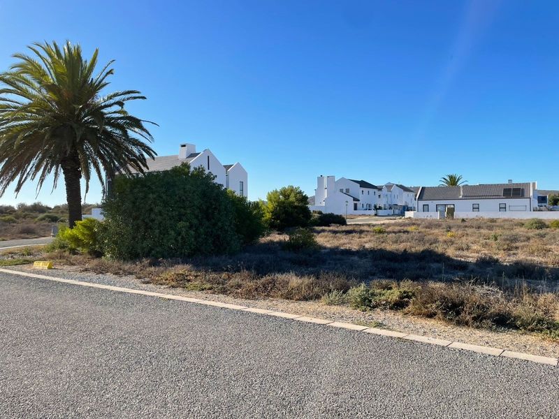 A view of a vacant residential plot situated in a developed neighborhood with paved road access and established landscaping.
