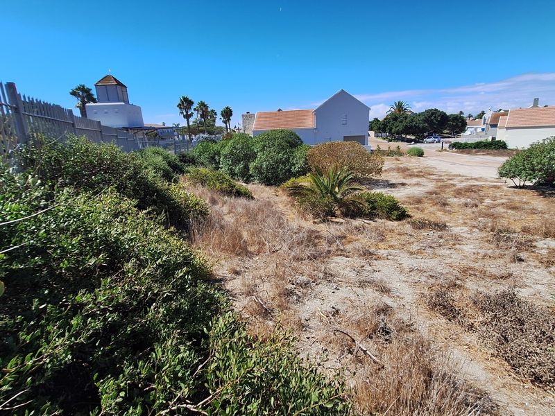 A view of a vacant residential plot featuring natural vegetation and perimeter fencing, situated within a developed neighborhood setting.
