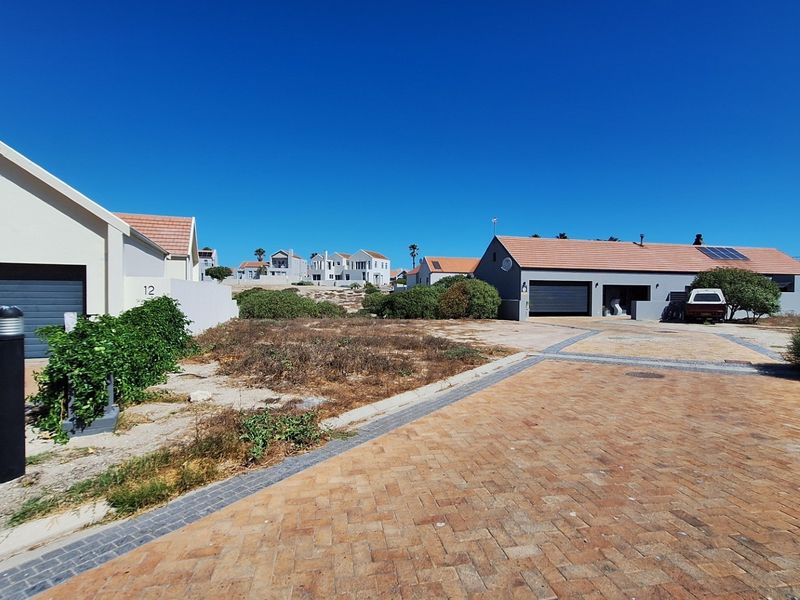 A view of a residential street featuring paved driveways, garage access, and surrounding properties in a coastal estate setting.