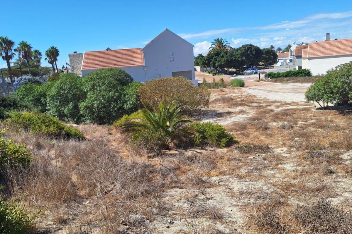 A vacant residential plot featuring natural vegetation, situated in a developed neighborhood with surrounding homes.
