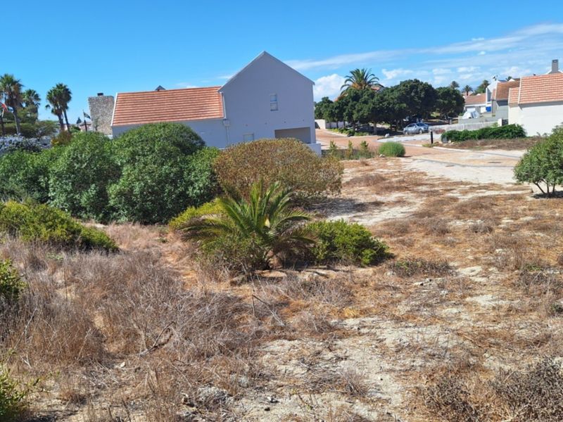 A vacant residential plot featuring natural vegetation, situated in a developed neighborhood with surrounding homes.