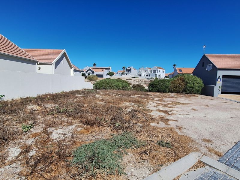 A vacant residential plot featuring a paved driveway, boundary wall, and adjacent garage structure in a developed neighborhood setting.