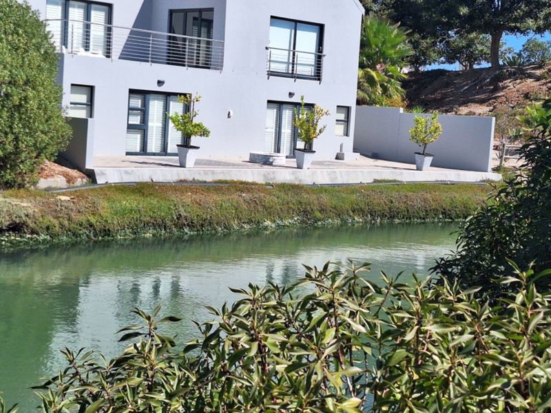 Rear view of a modern multi-story residence featuring a balcony and patio area overlooking a tranquil canal.