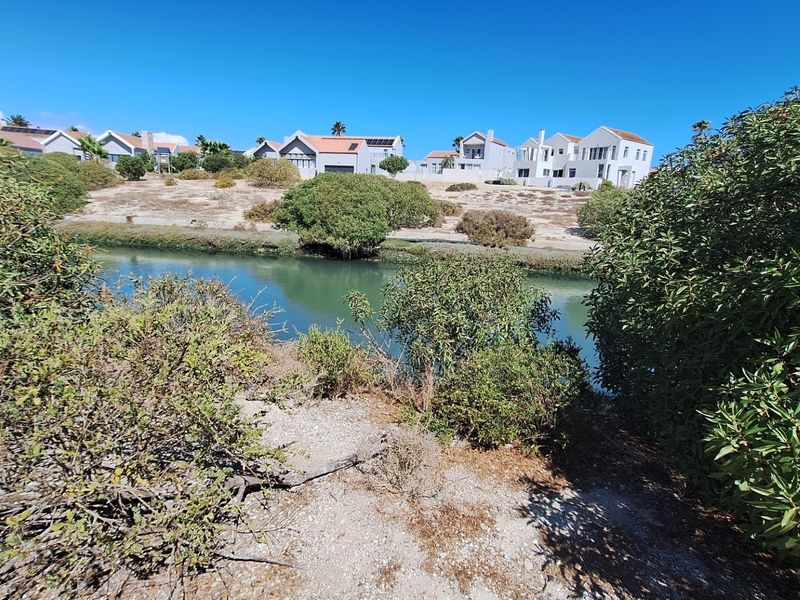 A scenic view of a natural waterway and surrounding coastal vegetation with residential properties visible in the background.