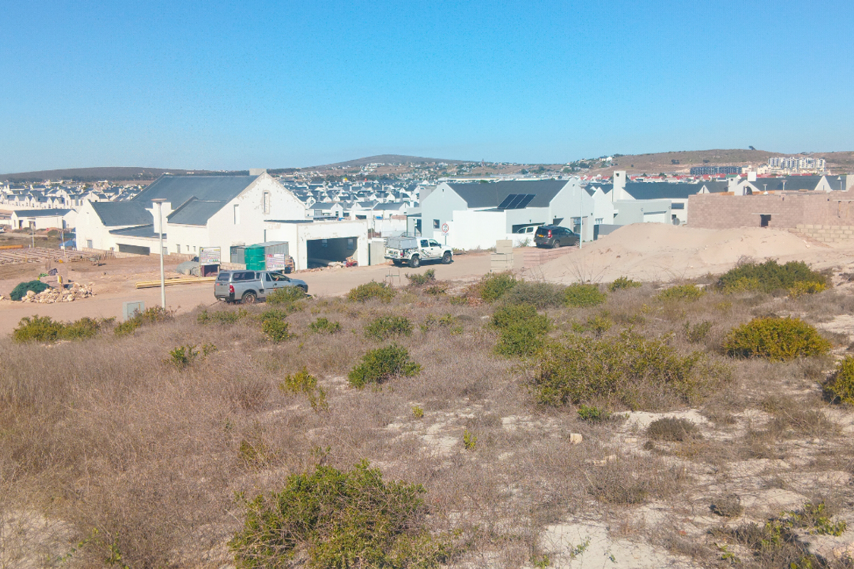 A view of an undeveloped residential plot featuring native vegetation with surrounding residential development in the background.