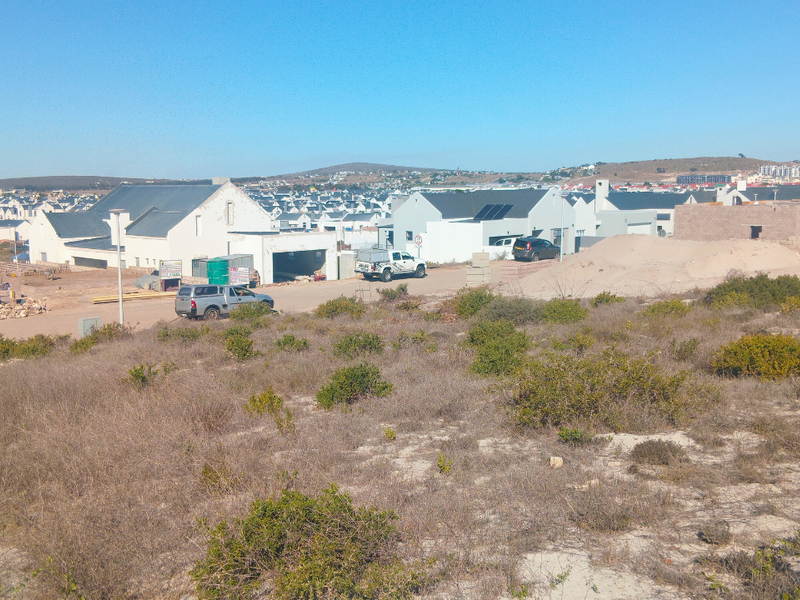 A view of an undeveloped residential plot featuring native vegetation with surrounding residential development in the background.