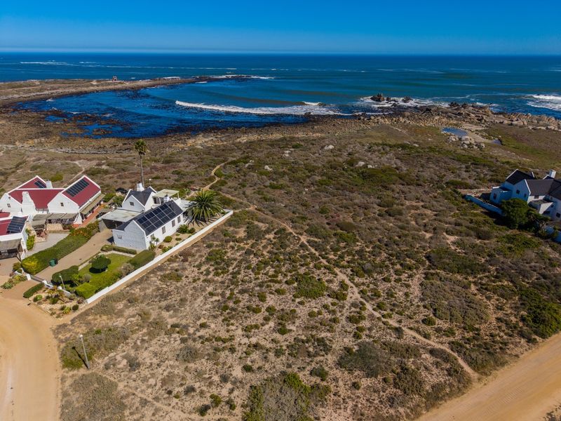 Aerial view of a vacant residential plot situated in a coastal setting, featuring natural vegetation and proximity to the ocean.