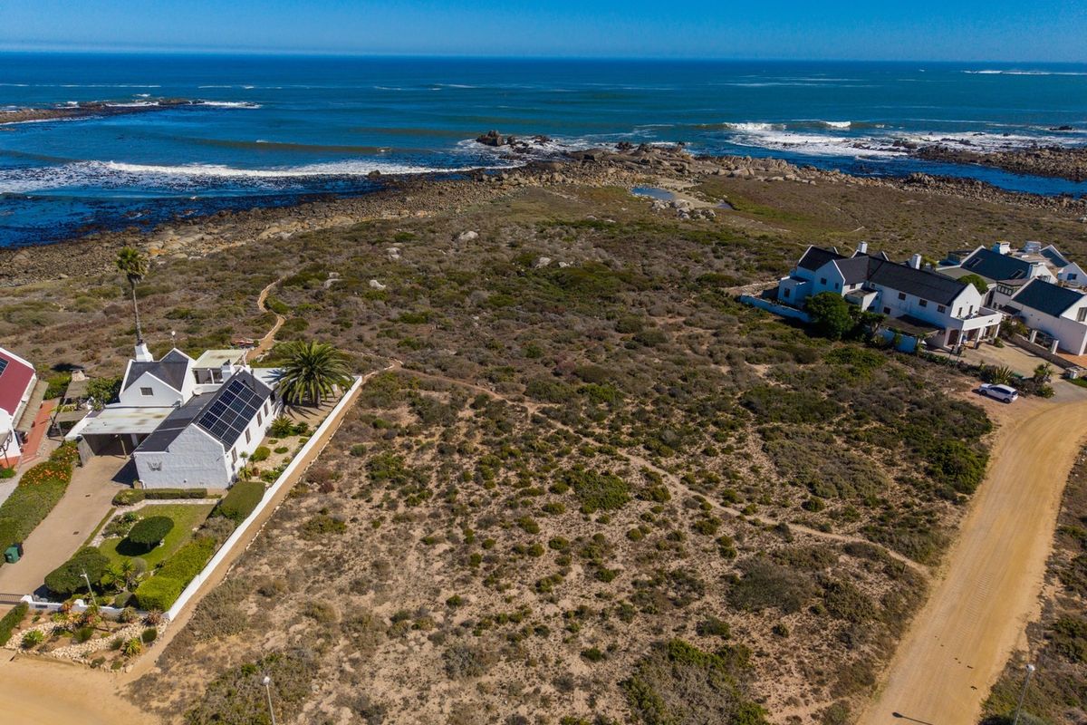 An aerial view of a vacant residential plot situated in a coastal setting, featuring natural vegetation and proximity to the ocean.