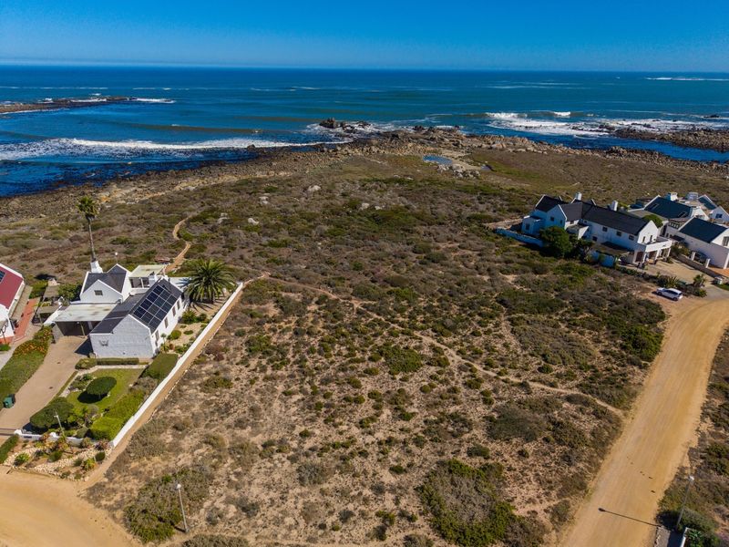 An aerial view of a vacant residential plot situated in a coastal setting, featuring natural vegetation and proximity to the ocean.