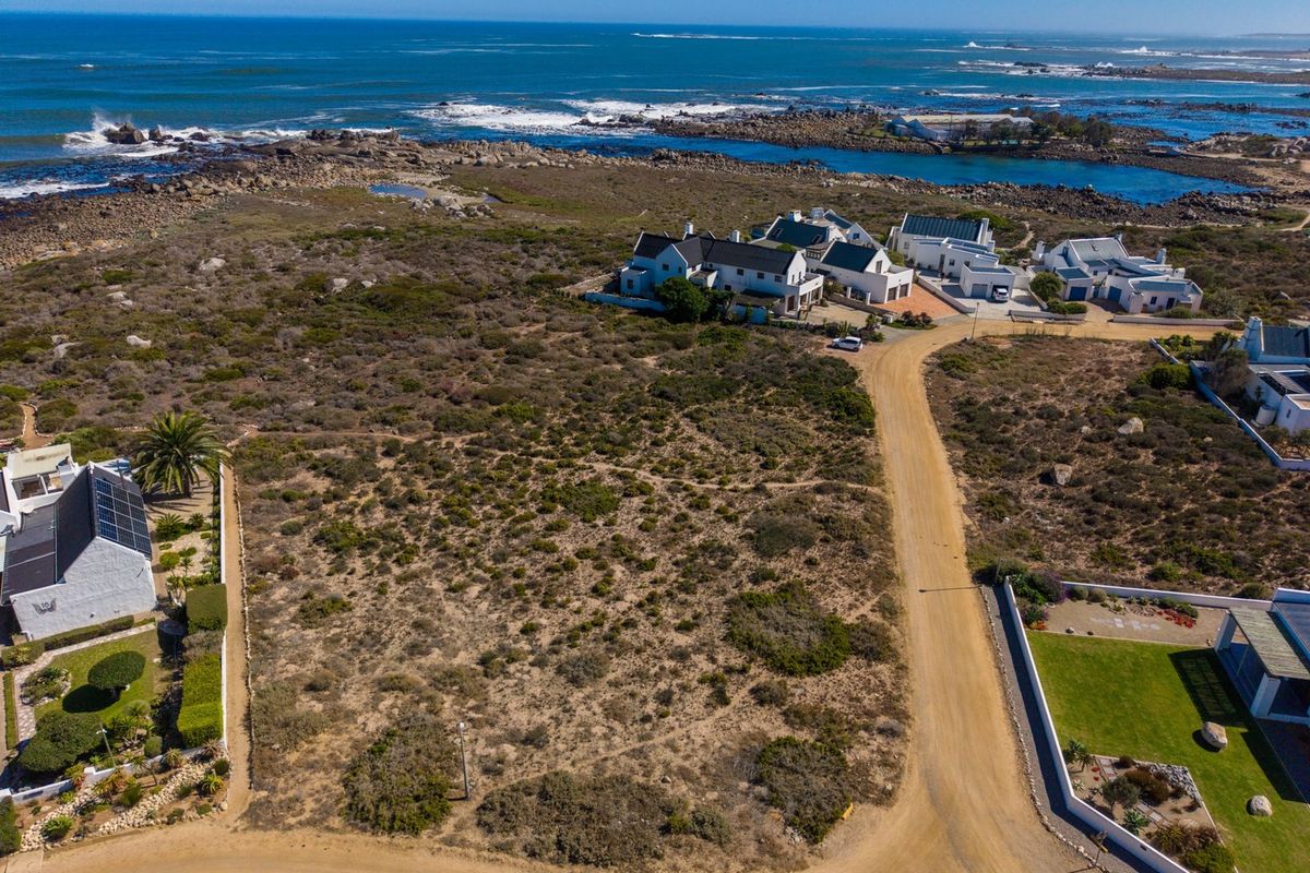 Aerial view of a vacant residential plot situated in a coastal estate, featuring natural vegetation and direct access to a dirt road.