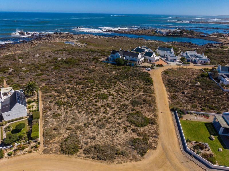 Aerial view of a vacant residential plot situated in a coastal estate, featuring natural vegetation and direct access to a dirt road.