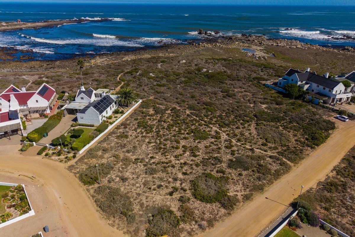 Aerial view of a vacant residential plot situated in a coastal estate, offering direct proximity to the ocean and surrounding established homes.