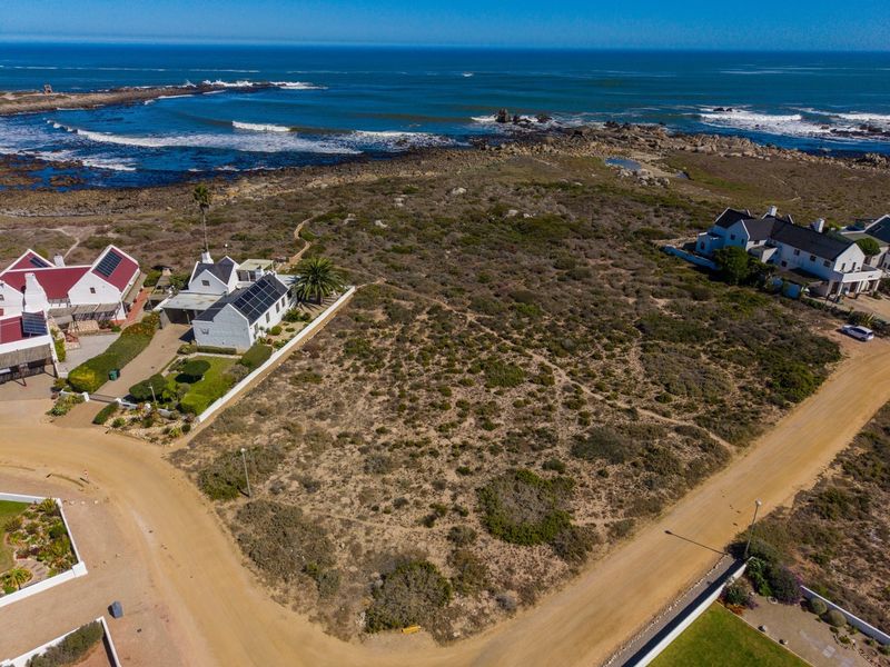 Aerial view of a vacant residential plot situated in a coastal estate, offering direct proximity to the ocean and surrounding established homes.