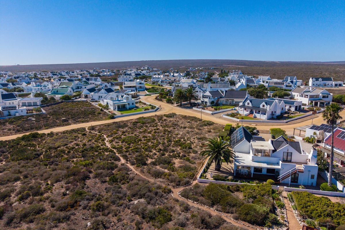 An aerial view of a coastal residential estate featuring white houses, solar panels, and surrounding natural landscape.