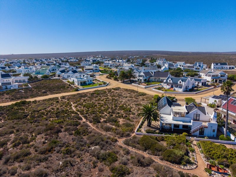 An aerial view of a coastal residential estate featuring white houses, solar panels, and surrounding natural landscape.