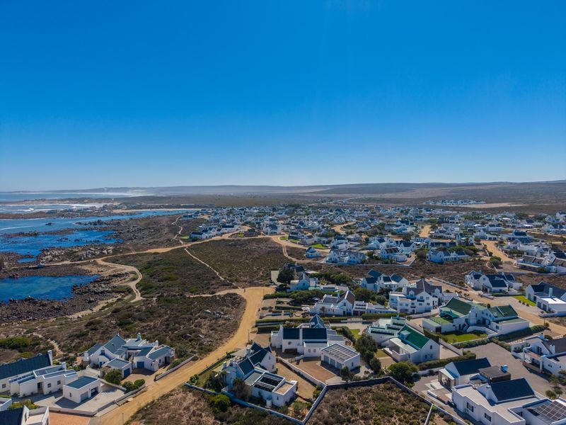 An aerial view of a coastal residential estate featuring white houses, natural vegetation, and proximity to the ocean.
