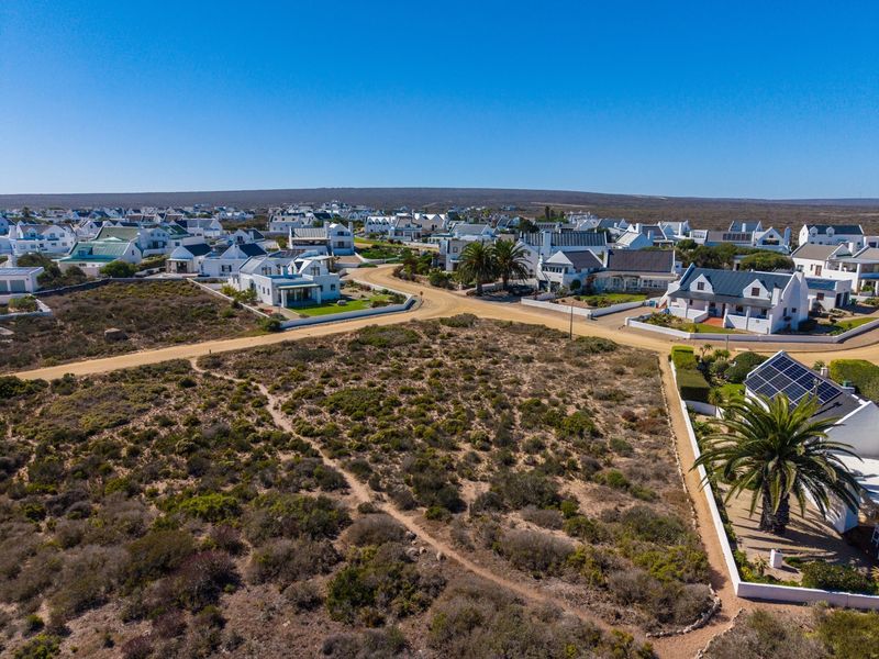 An aerial view of a vacant residential plot situated within a developed coastal neighborhood with established dirt road access.