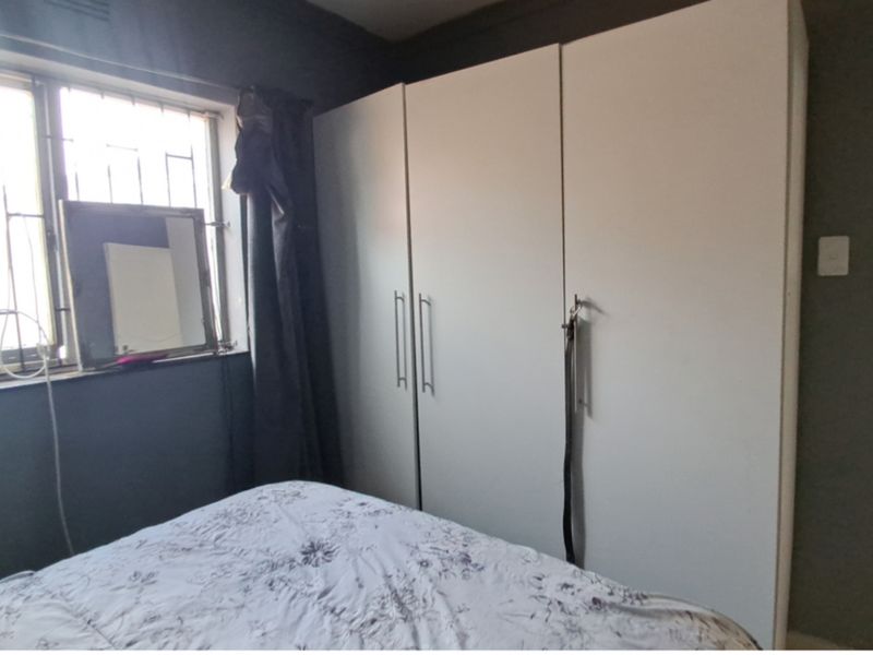 A bedroom featuring built-in cupboards, tiled flooring, and a window fitted with security bars.