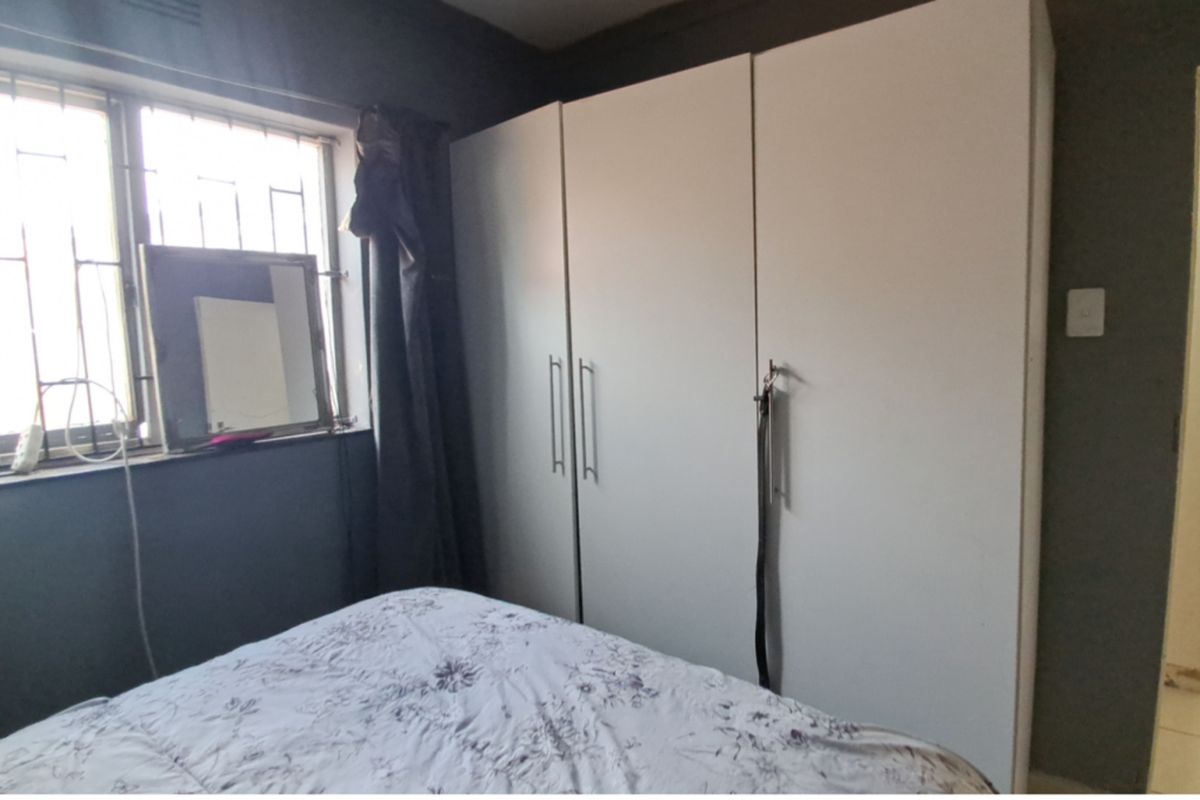 A bedroom featuring built-in cupboards, tiled flooring, and a window fitted with security bars.