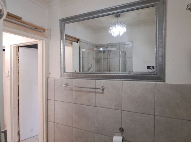 Bathroom featuring a shower enclosure, tiled walls, and a large wall mirror, currently requiring minor repairs to finishes and fixtures.