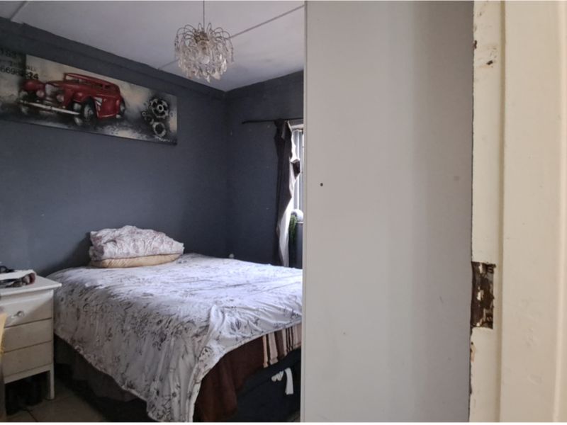 A bedroom featuring dark painted walls and a ceiling light fixture, showing visible wear to the door frame and surrounding wall plaster.
