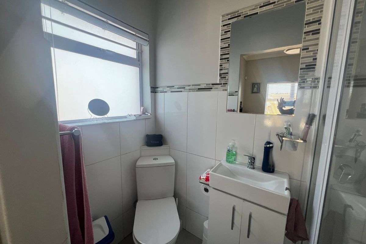 Compact bathroom featuring a white vanity cabinet, ceramic basin, toilet, and a shower enclosure with tiled walls and a decorative mosaic border.