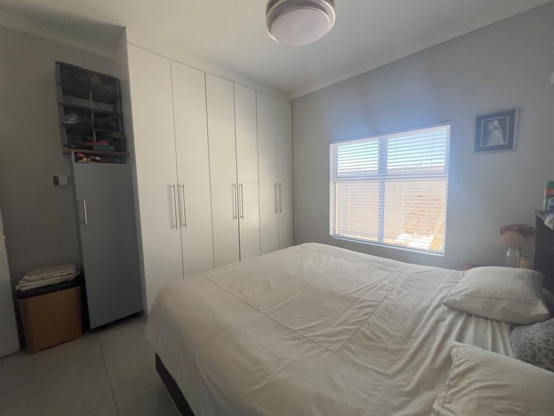 A well-maintained bedroom featuring built-in cupboards, tiled flooring, and natural light through a window fitted with venetian blinds.