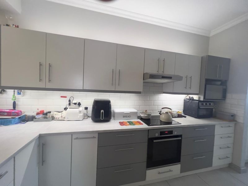 Modern kitchen featuring grey and white cabinetry, subway tile backsplash, integrated extractor fan, and built-in oven with electric hob.