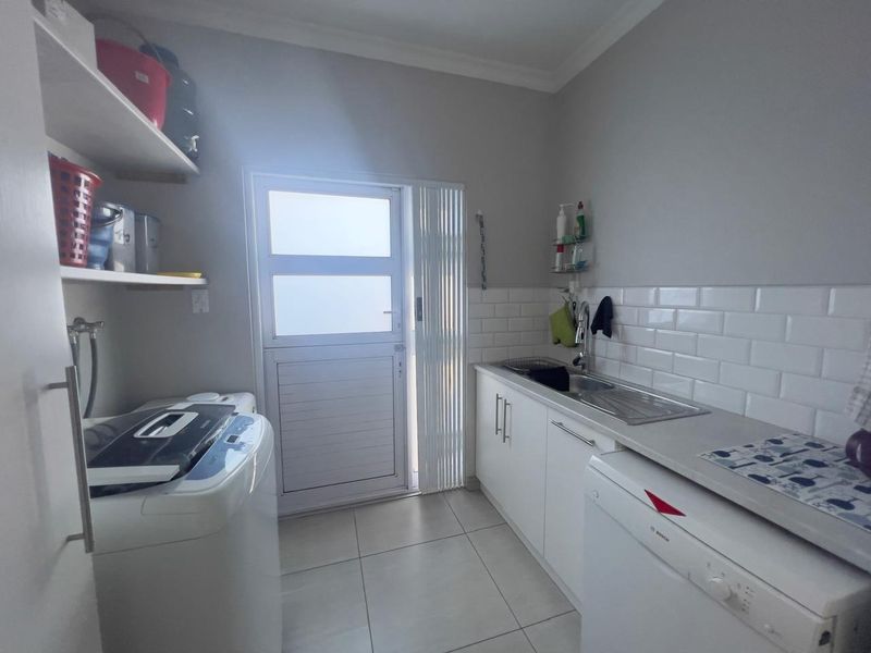 Functional laundry room featuring built-in cabinetry, a stainless steel sink, subway tile backsplash, and direct access to the exterior.