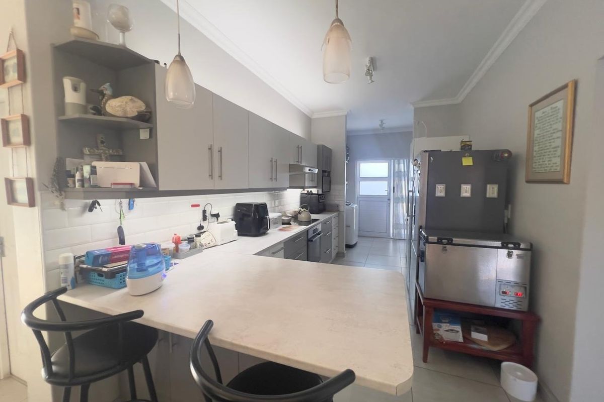 A functional kitchen featuring grey built-in cabinetry, a breakfast bar, subway tile backsplash, and integrated appliances with tiled flooring throughout.