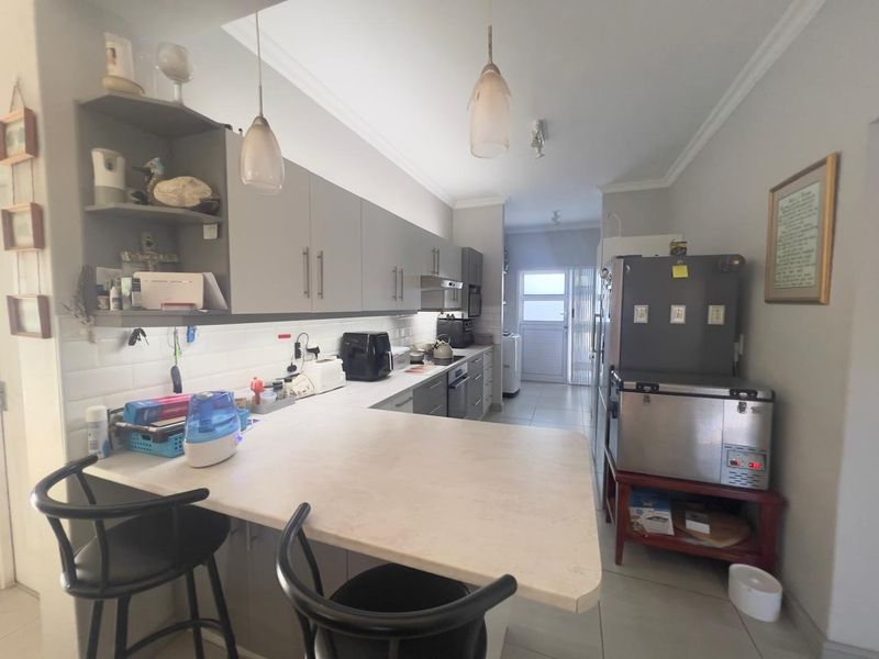 A functional kitchen featuring grey built-in cabinetry, a breakfast bar, subway tile backsplash, and integrated appliances with tiled flooring throughout.