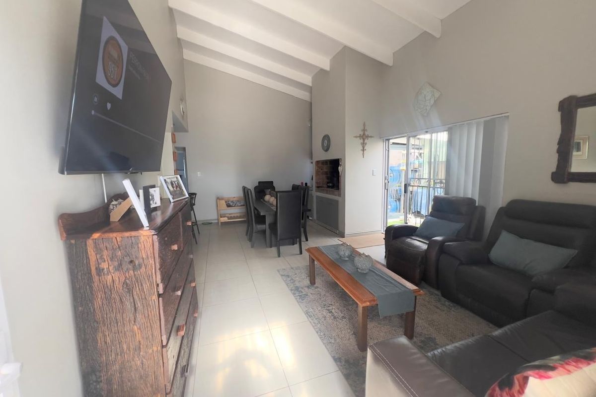 Spacious open-plan living and dining area featuring vaulted ceilings with exposed beams, tiled flooring, and a built-in fireplace with access to the patio.